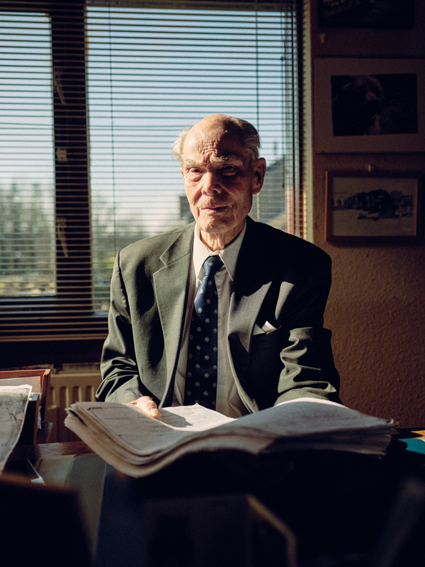 Sfeervolle documentaire fotografie voor jaarverslag van de Oorlogsgravenstichting. Portret van Tom Paulus in zijn werkkamer, omringd door archiefmateriaal, foto's en persoonlijke herinneringen uit de Tweede Wereldoorlog.